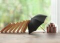 Black umbrella protectin stack of coins falling from a domino effect caused by wood sticks