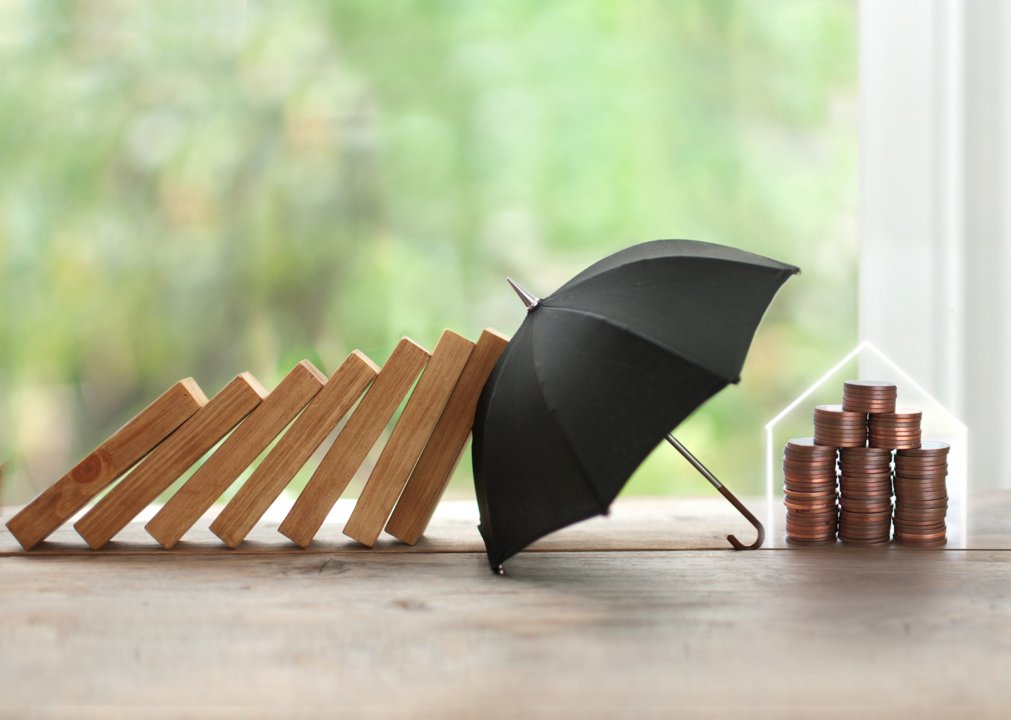 Black umbrella protectin stack of coins falling from a domino effect caused by wood sticks