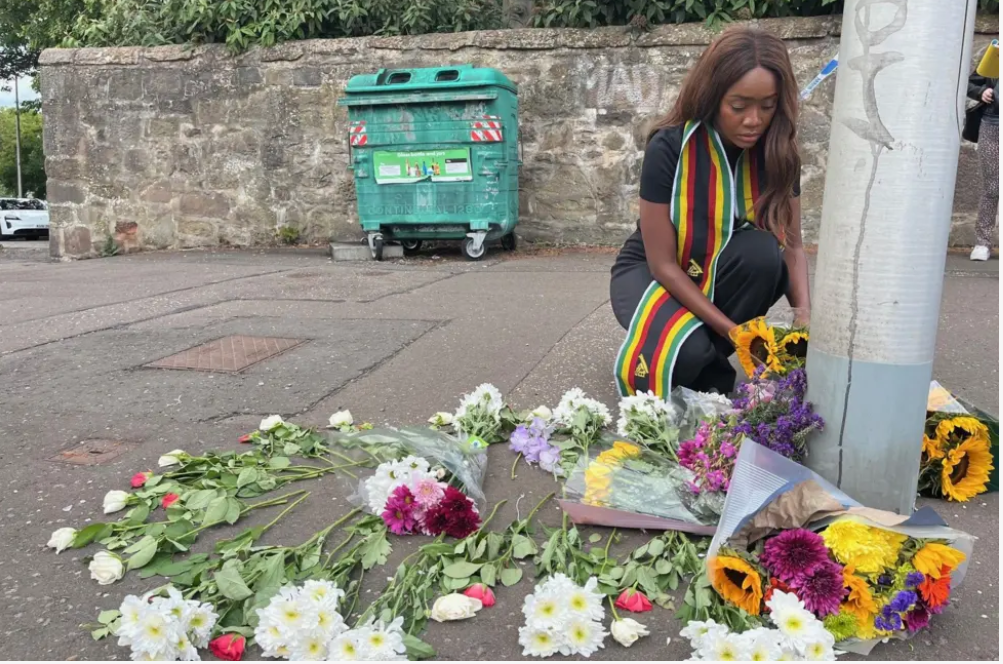 a local woman was seen laying flowers near a lamppost, her scarf bearing the colours of the Zimbabwean flag