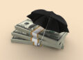 Stacks of money under an umbrella, symbolising how Diaspora Funeral Insurance offers protection that savings alone cannot provide.