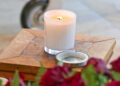 Lit memorial candle on a wooden table with flowers in the foreground, symbolising remembrance and funeral reflection.
