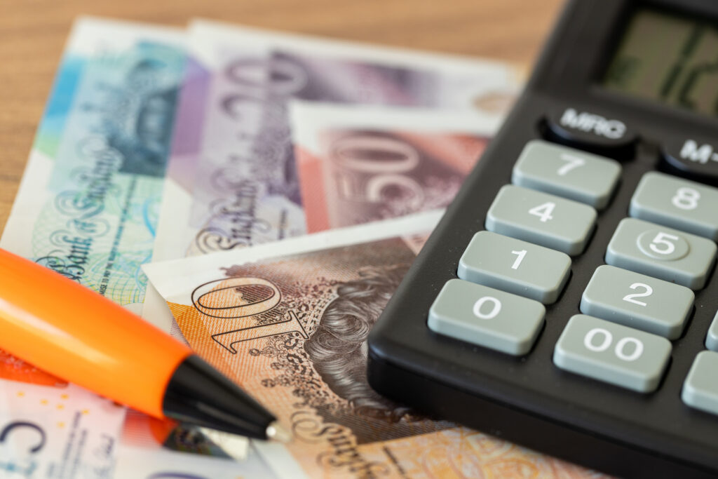 Close-up of British pound banknotes, an orange pen, and a calculator on a desk, illustrating money management and budgeting for Africans abroad. Top Financial Terms Every African in the Diaspora Should Know.