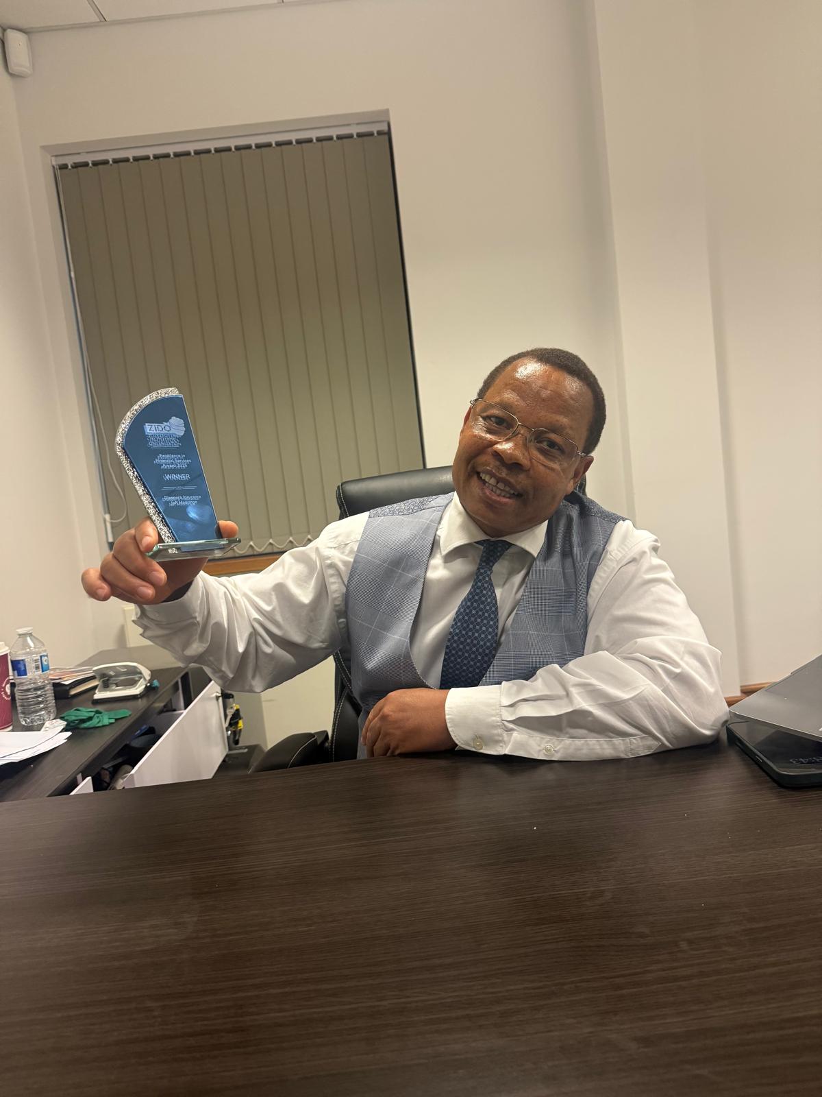Jeff Madzingo honoured for Empowering the African Diaspora. Jeff Madzingo, CEO of Diaspora Insurance, smiles while holding the ZIDO Excellence in Financial Services Award 2025 trophy in his office, celebrating his recognition for empowering the African diaspora.