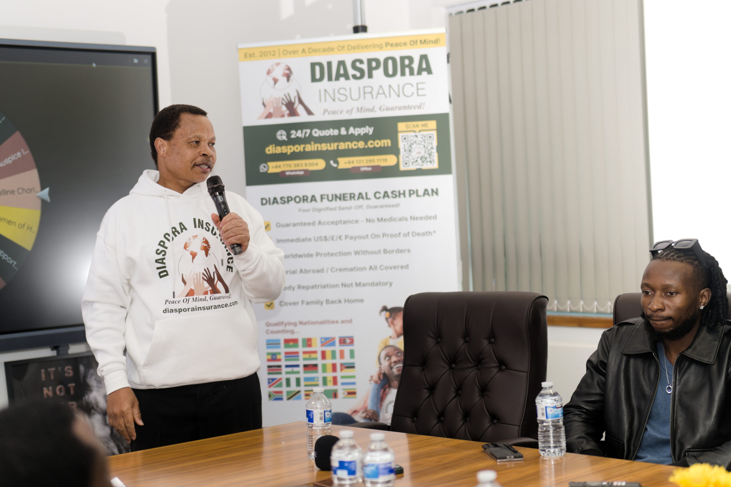 Jeff Madzingo, CEO of Diaspora Insurance, speaking at an event while musician Baba Harare looks on.