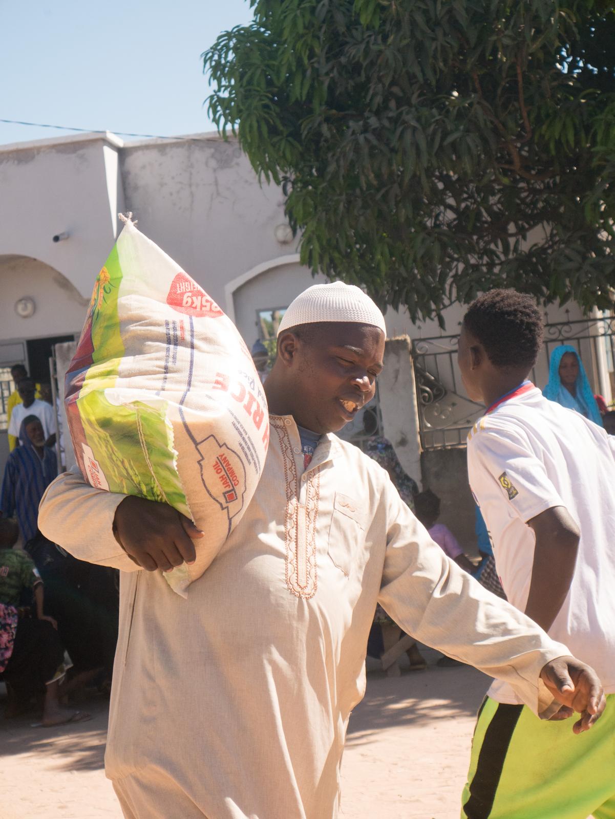 Smiling man carrying a bag of rice donated by Diaspora Insurance in Brikama Manduar, The Gambia.